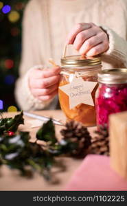 Putting Reusable Wooden Gift Tag On Homemade Jars Of Preserved Fruit For Eco Friendly Christmas Gift