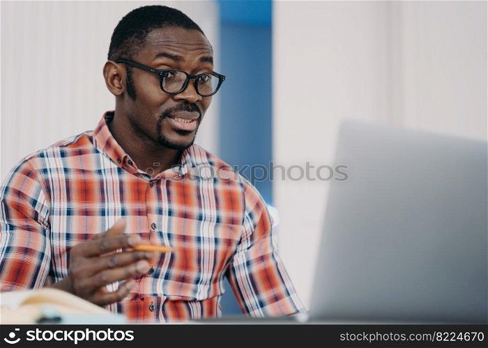 Puzzled african american employee in glasses looking at laptop screen shocked by breakdown of computer or problems in work. Outraged black male is perplexed by program error or bad internet connection. Puzzled african american employee in glasses looking at laptop screen shocked by problems in work