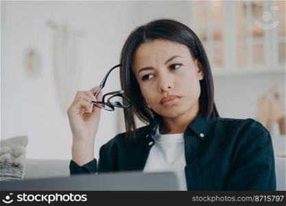 Puzzled businesswoman working on business project at laptop took off glasses, thinking about problem. Tired overworked female holding eyeglasses looking aside pondering, answering email.. Puzzled businesswoman working on business project at laptop took off glasses, thinking about problem