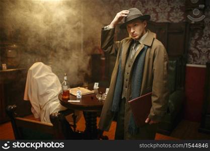 Puzzled detective in coat and hat, victim under the cape at the crime scene, retro style. Criminal investigation, inspector is working on a murder, vintage room interior on background. Puzzled detective in coat and hat, crime scene