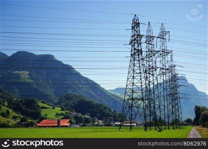 Pylon and electrical wire on the green farm field and road in Switzerland
