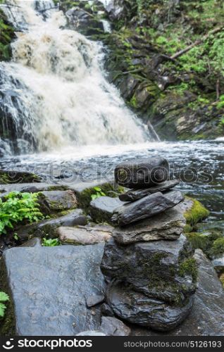 Pyramid of stones on the river bank with a waterfall