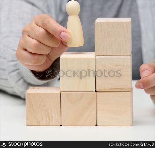 pyramids from wooden cubes and figurines of men on the table. The concept of achieving goals, moving up the career ladder. Detection of single-minded personality