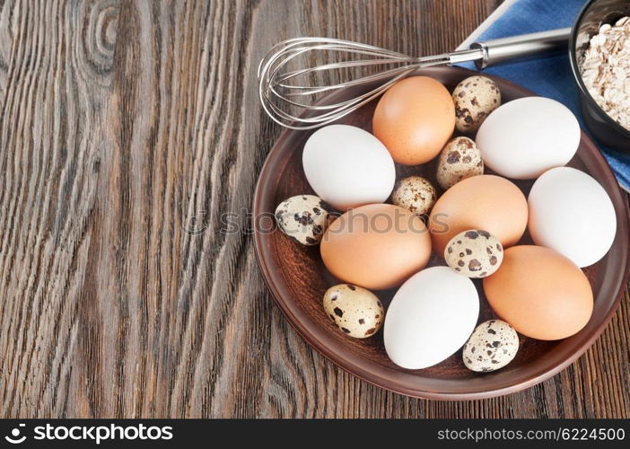 Quail and chicken eggs in a clay plate on a wooden background