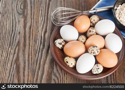 Quail and chicken eggs in a clay plate on a wooden background