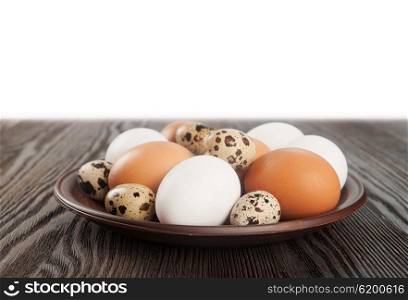 Quail and chicken eggs in a clay plate on a wooden table