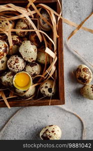 Quail eggs. Flat lay composition with small quail eggs in the wooden box on the concrete background. One broken egg with a bright yolk. Quail egg farm