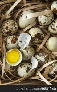 Quail eggs. Flat lay composition with small quail eggs on the natural wooden background. One broken egg with a bright yolk. Quail egg farm