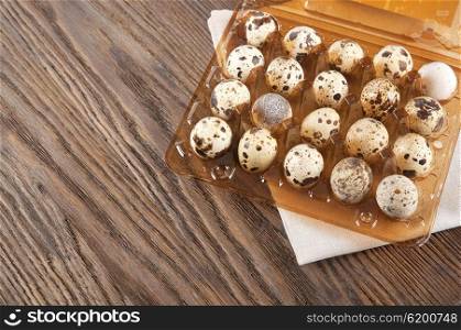 Quail eggs in a plastic box on a wooden background