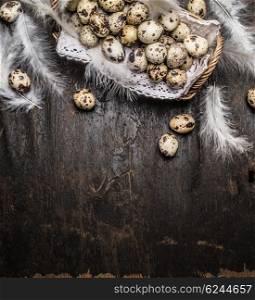 Quail eggs in basket with feathers on rustic wooden background, top view, vertical, place for text.