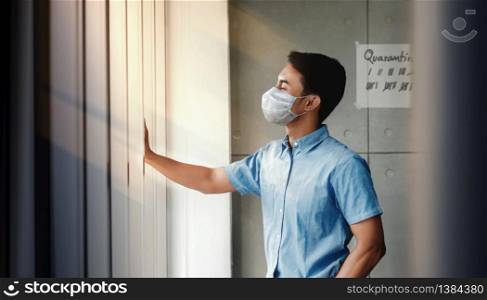 Quarantine at Home for Covid-19 Concept. Young Man with Surgical Mask Standing by Window in the House. Waiting to go Outside. Positive Mind