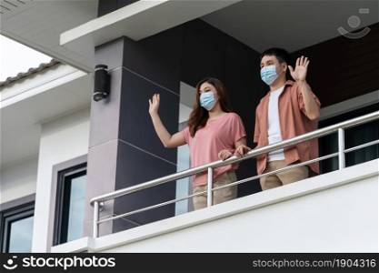 quarantine couple wearing a face mask and greeting neighbors from balcony of the home, coronavirus(covid-19) pandemic