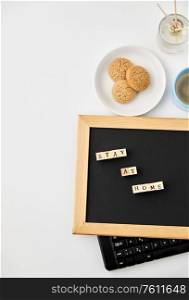 quarantine, epidemic and safety concept - close up of chalkboard with stay at home words on wooden toy blocks, coffee cup, cookies and book with aroma reed diffuser on white background. chalkboard with stay at home words on toy blocks