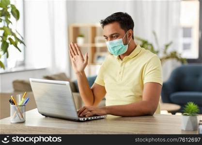 quarantine, remote job and pandemic concept - indian man wearing face protective medical mask for protection from virus disease with laptop computer having video call at home office. man in mask with laptop having video call at home