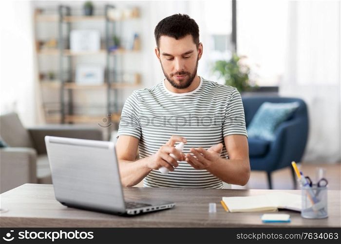 quarantine, remote job and pandemic concept - man with laptop computer using hand sanitizer working at home office. man using hand sanitizer at home office