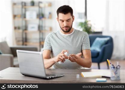 quarantine, remote job and pandemic concept - man with laptop computer using hand sanitizer working at home office. man using hand sanitizer at home office