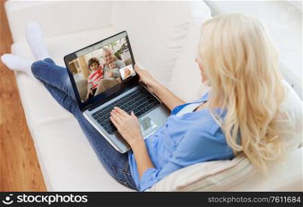 quarantine, technology and online communication concept - young woman with laptop computer sitting on couch at home and having video call with family. woman with laptop having video call with family