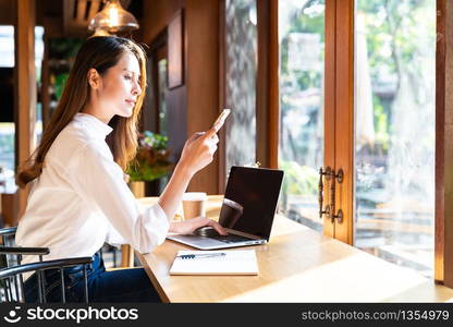 Quarantine Young asian woman wearing smart casual clothes work at home in living room using laptop and drinking hot coffee and croissant while city lockdown for covid-19 corona virus pandemic.