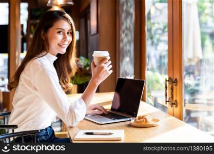 Quarantine Young asian woman wearing smart casual clothes work at home in living room using laptop and drinking hot coffee and croissant while city lockdown for covid-19 corona virus pandemic.