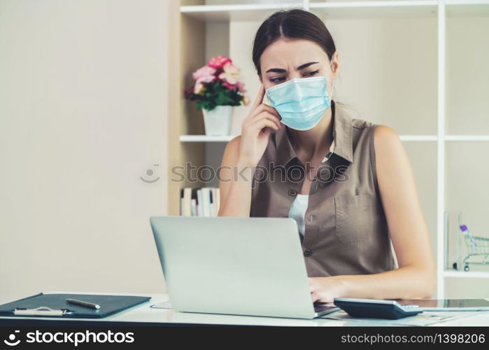 Quarantined woman working at home wearing face mask protect from Coronavirus. Concept of social distancing to stop spreading of Coronavirus Disease or COVID-19.