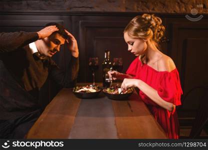Quarrel of young couple in restaurant, bad evening. Elegant woman in red dress and her man eating in cafe