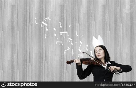 Queen of performance. Young pretty businesswoman in paper crown playing violin