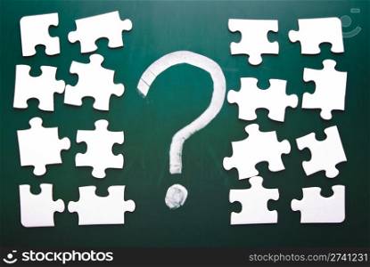Question mark and puzzle pieces on blackboard
