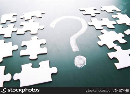 Question mark and puzzle pieces on blackboard