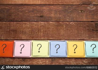 question mark concept - handwriting in black ink on colorful sticky notes against rustic wood with a copy space