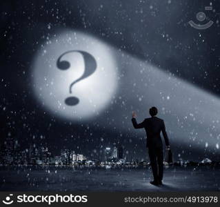 Question mark in spotlight. Businessman standing with back and looking at question mark concept