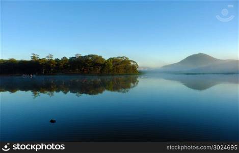 Quiet, calm and peaceful scenery of Than Tho lake, Da Lat city, Viet Nam in early morning, pine tree in forest reflect on water make romantic and fresh view for ecotourism in summer