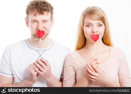 Quietly about love and feelings. Lovely charming blonde female and male lovers covering their mouth by little small heart on stick.. Lovely couple covering their mouth by heart.