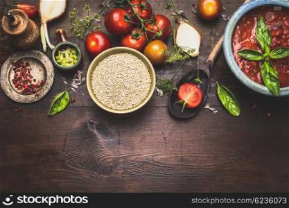 Quinoa in bowl with wooden spoon and vegetables and seasoning cooking ingredients on rustic background, top view