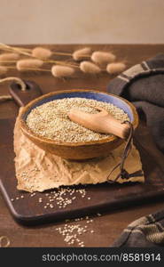 Quinoa in ceramic bowl with wooden scoop on rustic countertop.