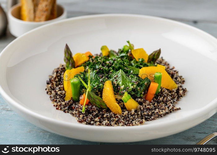 Quinoa salad with orange and kale leaves on white porcelain plate on wooden table