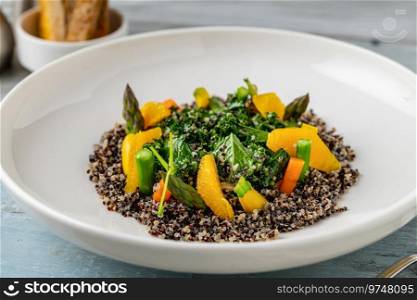 Quinoa salad with orange and kale leaves on white porcelain plate on wooden table