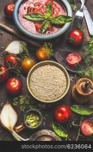 Quinoa seeds on dark kitchen table with vegetables cooking ingredients and tomatoes sauce, top view. Superfood and Healthy or Vegan food concept