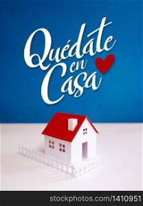"Quote in spanish "quedate en casa" (Stay at Home) on blue background with little paper house. Social distancing campaign during quarentine COVID-19 pandemic"