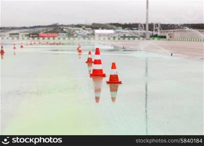 racing, motosports, extreme and motoring concept - traffic cones and sprinklers on wet speedway of stadium