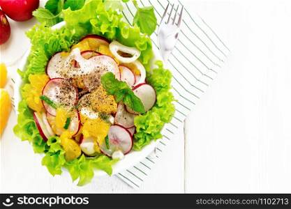 Radish, onion and orange salad with mint, vegetable oil and spices on lettuce in a plate on a towel on wooden board background from above