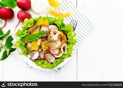 Radish, onion and orange salad with mint, vegetable oil and spices on lettuce in a plate on a napkin on wooden board background from above