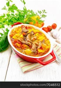 Ragout of turkey meat, tomato, yellow sweet pepper and onion with sauce in a brazier on a towel on the background of a wooden board