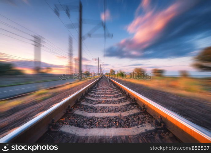 Railroad and beautiful blue sky with clouds at sunset with motion blur effect in summer. Industrial landscape with railway station and blurred background. Railway platform in speed motion. Concept. Railroad and sky with clouds at sunset with motion blur effect