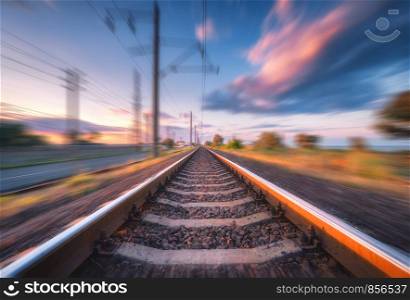 Railroad and beautiful blue sky with clouds at sunset with motion blur effect in summer. Industrial landscape with railway station and blurred background. Railway platform in speed motion. Concept. Railroad and sky with clouds at sunset with motion blur effect
