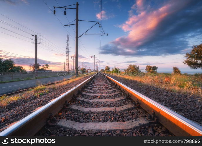 Railroad and beautiful sky at sunset in summer. Rural industrial landscape with railway station, blue sky with colorful clouds and orange sunlight, road. Railway platform. Sleepers. Heavy industry.. Railroad and beautiful sky at sunset in summer. Industrial