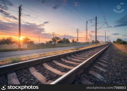 Railroad and beautiful sky at sunset in summer. Rural industrial landscape with railway station, blue sky with colorful clouds and orange sunlight, road. Railway platform. Sleepers. Heavy industry.. Railroad and beautiful sky at sunset in summer. Industrial