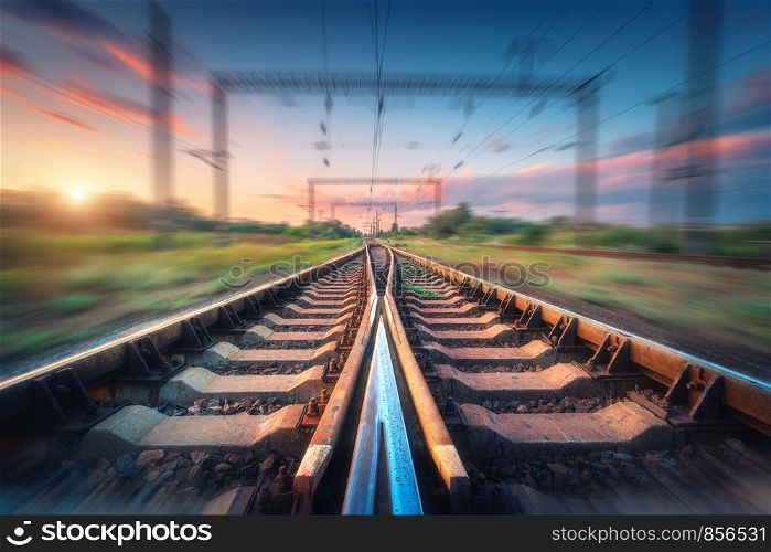 Railroad and beautiful sky at sunset with motion blur effect in summer. Industrial landscape with railway station and blurred background with colorful sky. Railway platform in speed motion. Sleepers