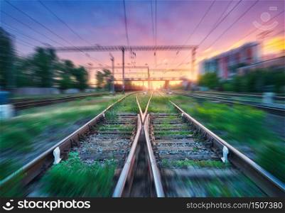 Railroad and beautiful sky with clouds at sunset with motion blur effect in summer. Industrial landscape with freight train, railway station and blurred background. Railway platform in speed motion