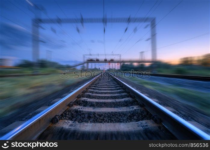 Railroad and blue sunset sky with clouds with motion blur effect. Industrial landscape with railway station and blurred background at twilight. Railway platform in move. Transportation. Speed motion. Railroad and blue sunset sky with clouds with motion blur effect