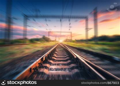 Railroad and colorful blue sky with clouds at sunset with motion blur effect in summer. Industrial landscape with railway station and blurred background. Railway platform in speed motion. Concept